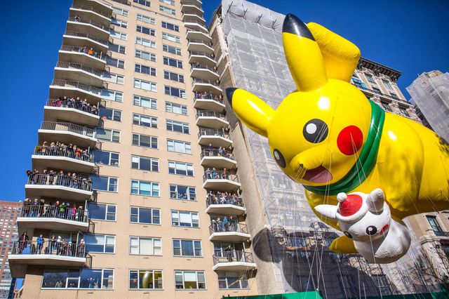 A Pikachu balloon floats in the air as residents look on from an apartment's balconies